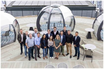 A group portrait of people standing outdoors on a wooden deck, near glass domes.