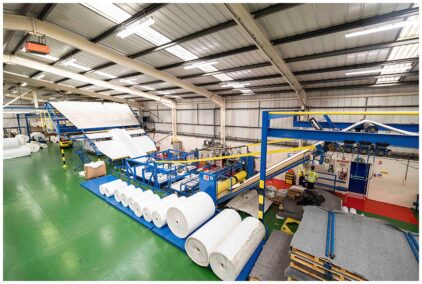 Indoor image of a large industrial warehouse with rolls of material and machinery.