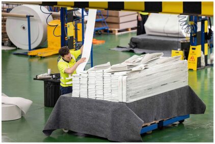 An indoor scene of a worker handling large stacks of materials in a factory setting.