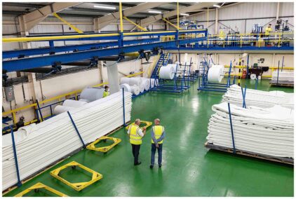 Indoor image of a factory with large rolls of material and workers in high-visibility vests.