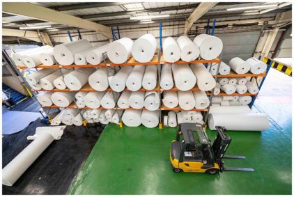 An indoor image of a warehouse with large rolls of material stacked on shelves and a forklift nearby.