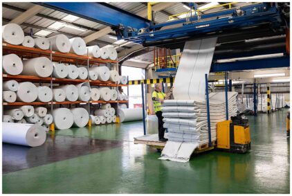 Indoor image of a factory with large rolls of paper and machinery.